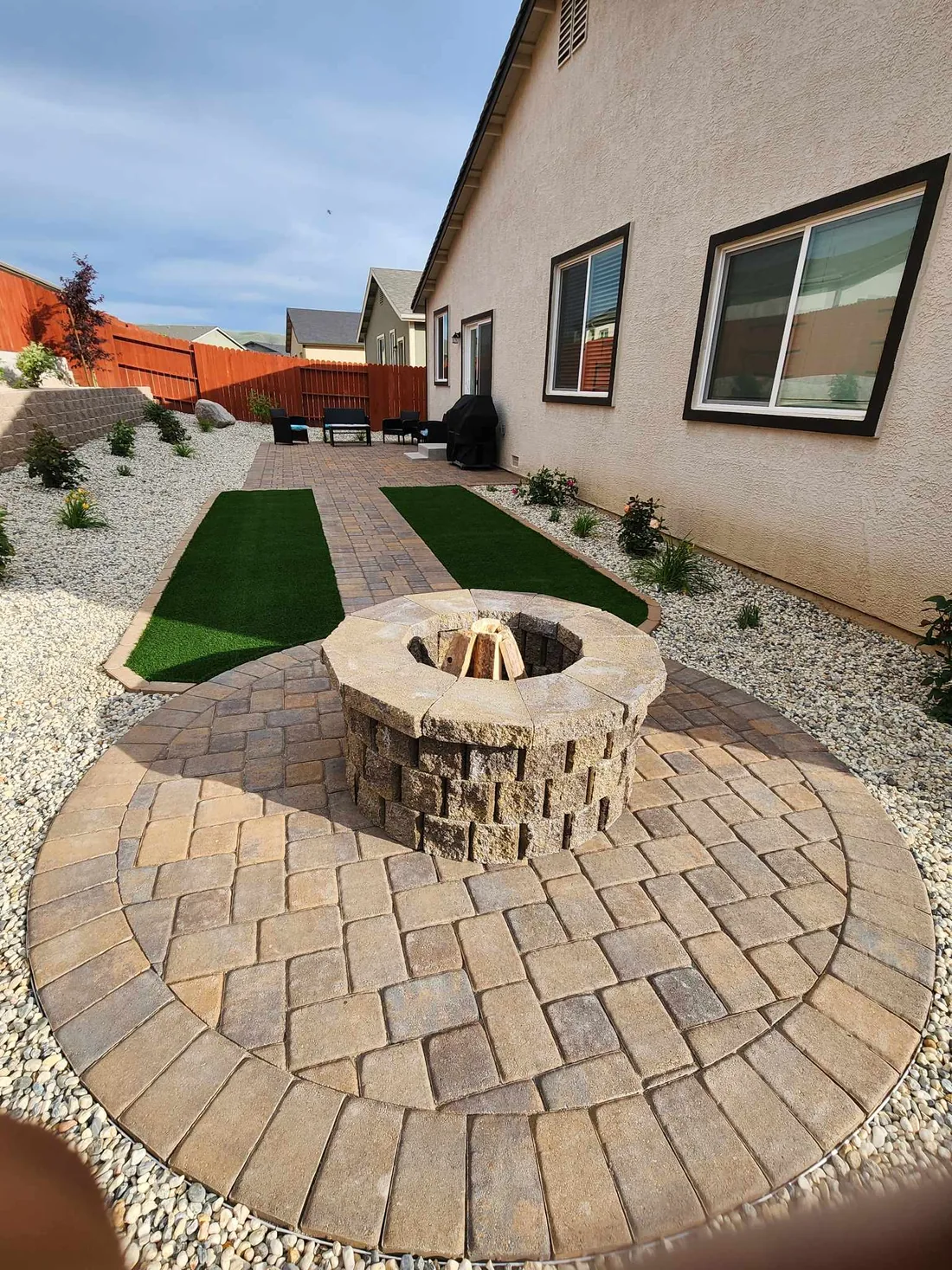 Backyard paver patio with a circular stone fire pit and a strip of turf in a Reno residential yard
